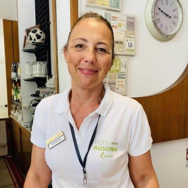 Receptionist dell'Hotel Ausonia a Rimini, indossa una maglietta bianca con il logo dell'hotel.